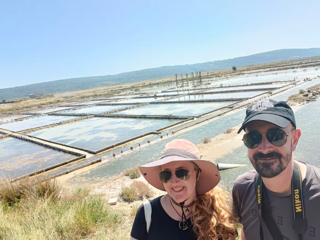 Couple standing in front of scenic salt pans under sunny blue sky.