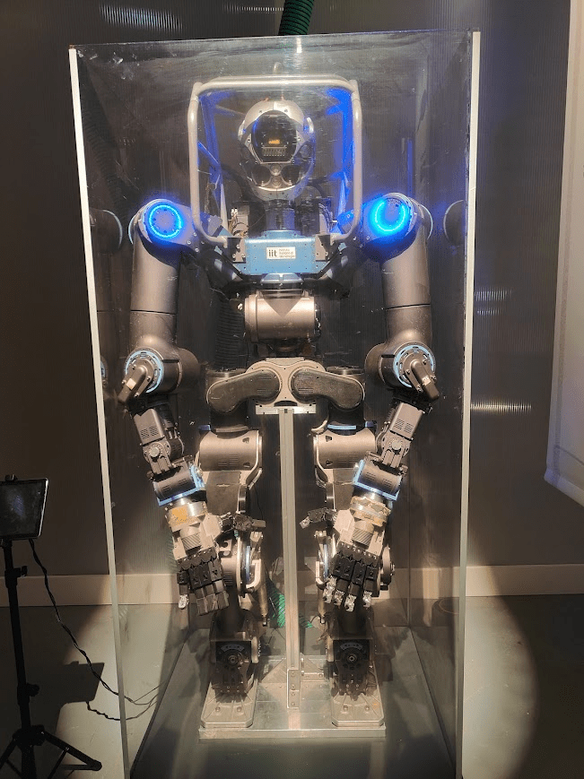 A humanoid robot displayed in a glass case, featuring illuminated blue accents and articulated limbs.